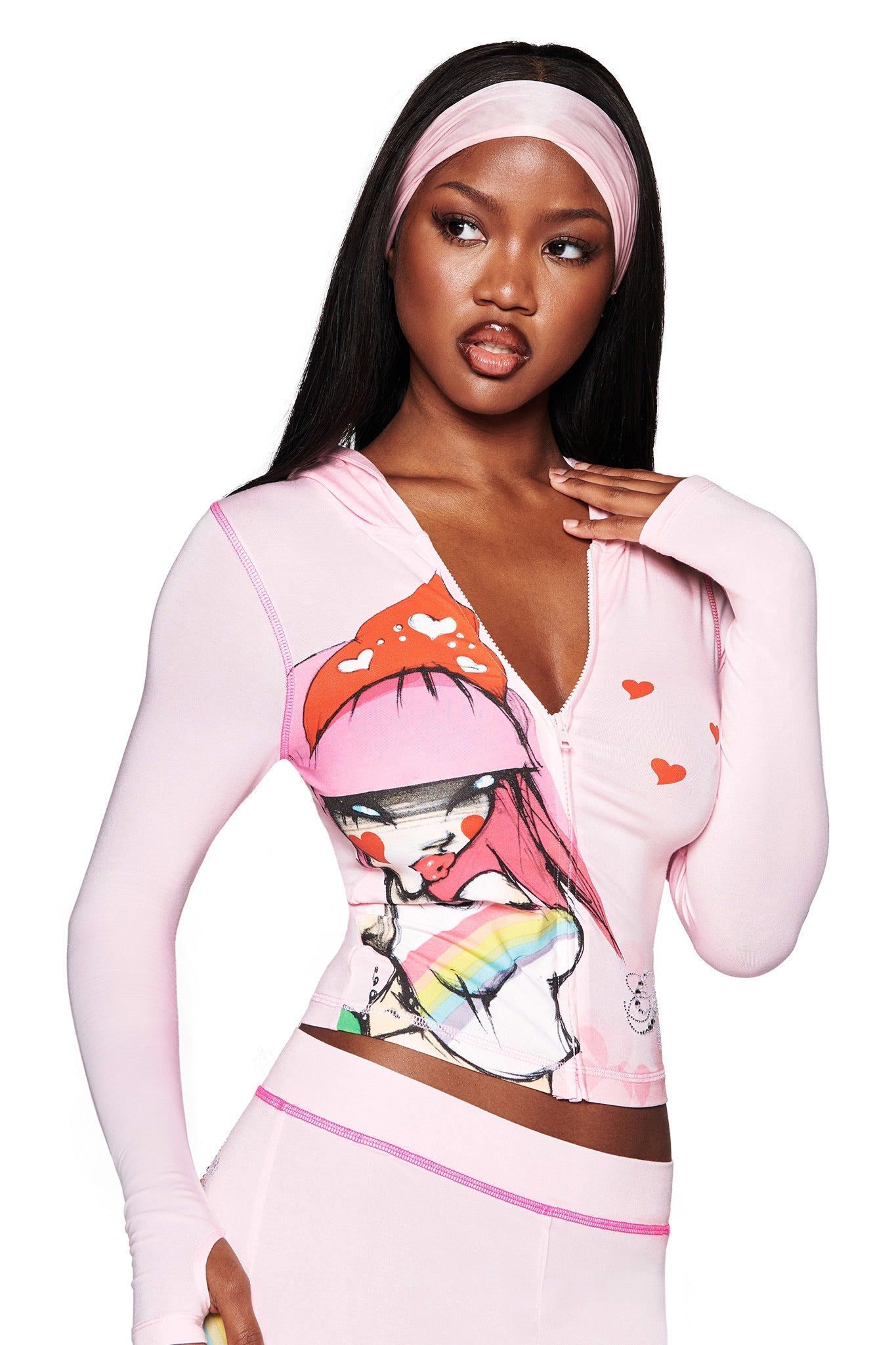 A woman poses against a white background, wearing an I.AM.GIA FAFI BLARE HOODIE in baby pink with diamanté details, a matching headband, and colorful cartoon graphics with red hearts.