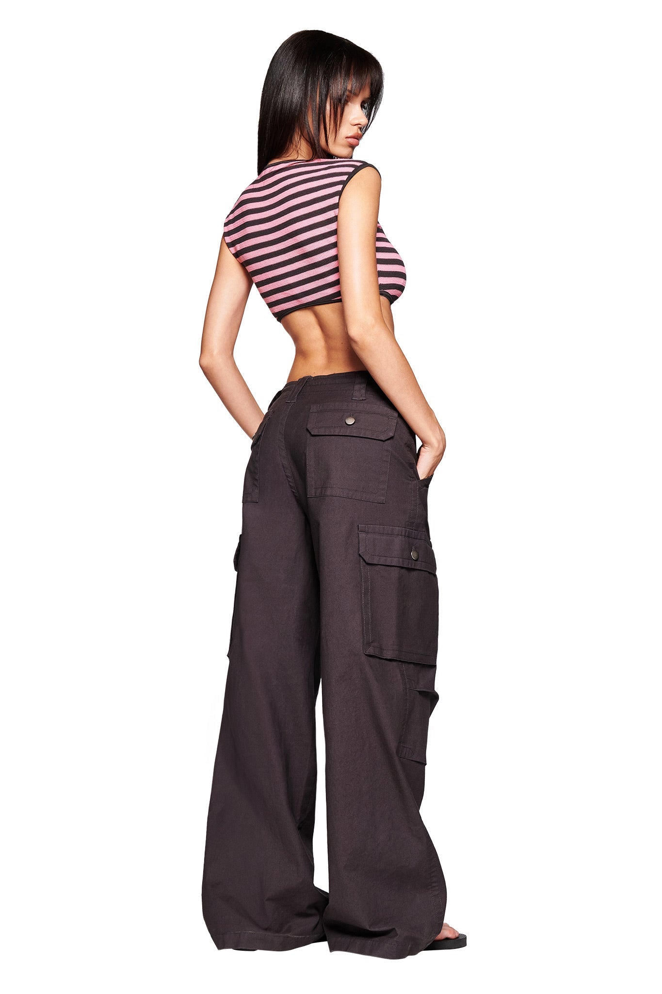 A woman with her back turned wears a sleeveless striped crop top and I.AM.GIA’s JAXXON PANT in grey, featuring a baggy leg silhouette and multiple pockets, against a white background.