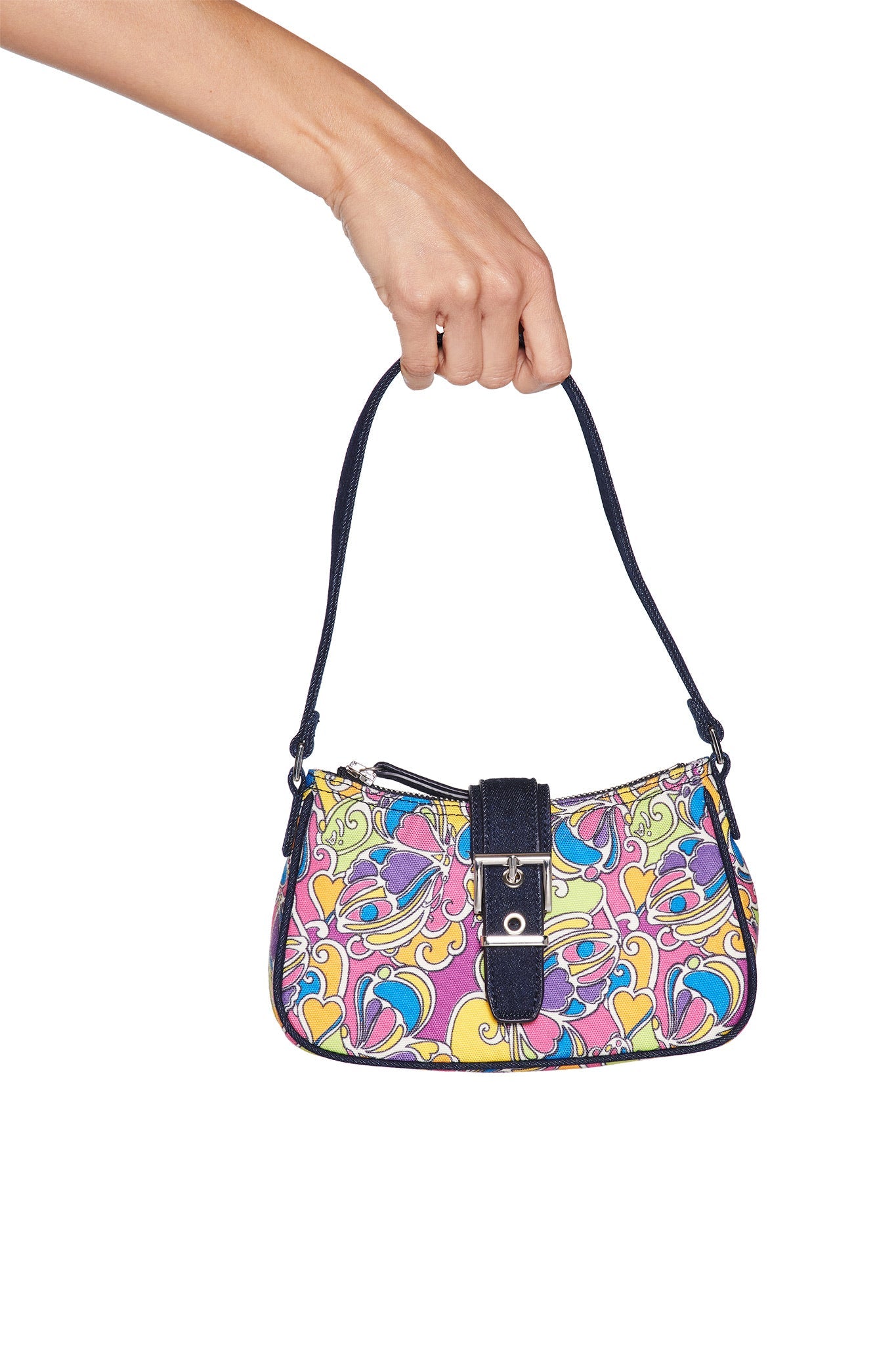 A hand holds the I.AM.GIA LILLIA BAG - TROPICAL BUTTERFLY BLOOM, featuring a vibrant abstract floral design, dark blue strap and buckle, set against a plain white background.