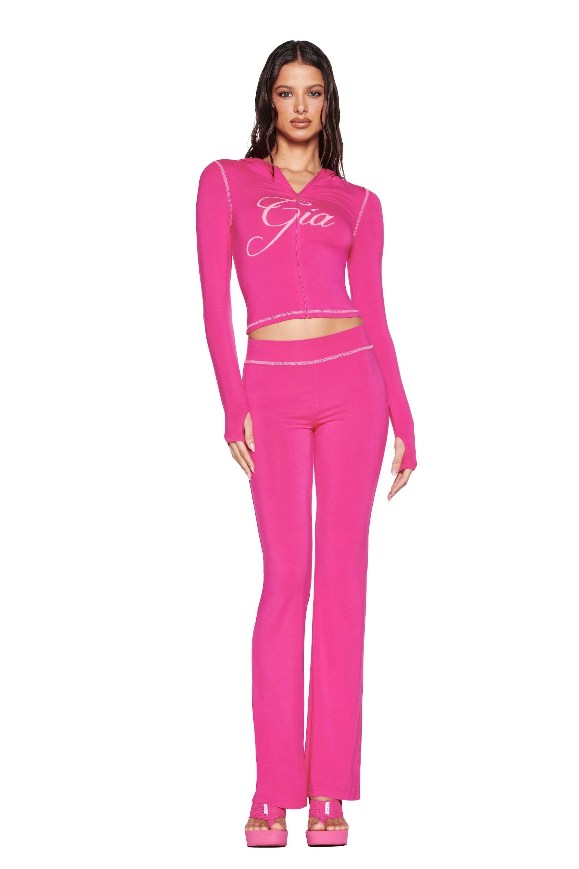 A woman faces forward in a hot pink I.AM.GIA "Gia" logo crop top, matching BLARE TRACKPANT - HOT PINK track pants by I.AM.GIA, and platform heels, standing against a white background.