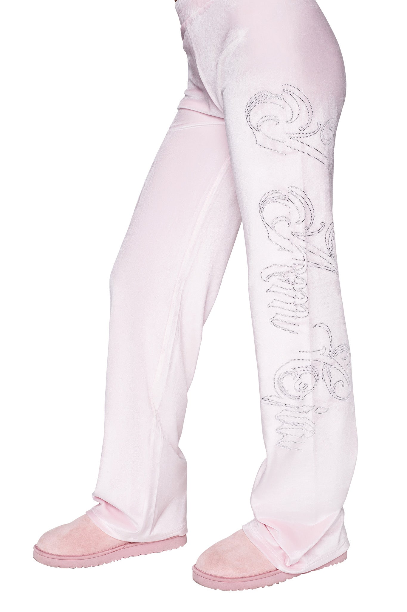 A person wearing light pink I.AM.GIA DARIA PANT - PINK : ICY PINK with intricate writing on one leg and matching pink slippers. The photo captures the pants from the waist down to the ankles, showcasing the soft and comfortable fabric.